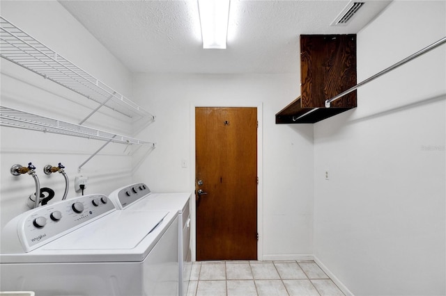 washroom with washing machine and clothes dryer, a textured ceiling, and light tile patterned flooring