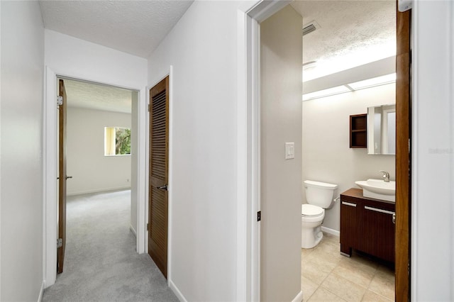 corridor featuring light carpet, a textured ceiling, and sink