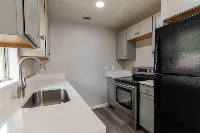 kitchen with hardwood / wood-style floors, black fridge, sink, stainless steel electric range oven, and a textured ceiling