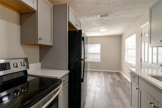 kitchen with a textured ceiling, black fridge, electric stove, and light wood-type flooring