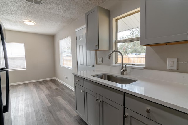 kitchen with gray cabinetry, sink, stainless steel fridge, light wood-type flooring, and a textured ceiling