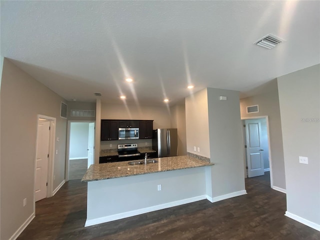 kitchen with light stone counters, sink, kitchen peninsula, dark wood-type flooring, and appliances with stainless steel finishes