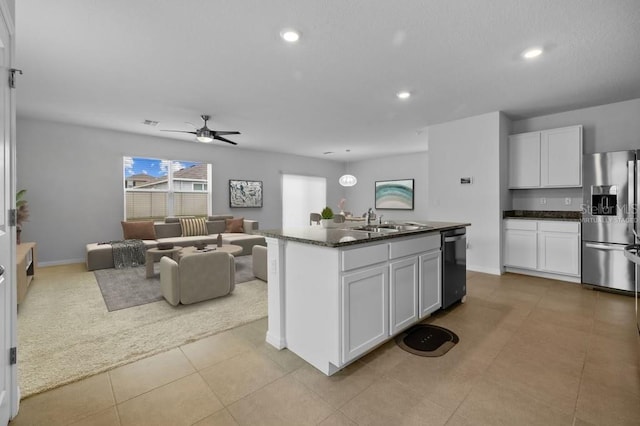 kitchen featuring ceiling fan, dark stone counters, an island with sink, appliances with stainless steel finishes, and white cabinetry