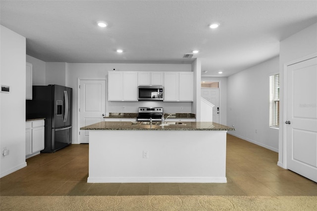 kitchen featuring a kitchen island with sink, appliances with stainless steel finishes, dark stone counters, and white cabinetry