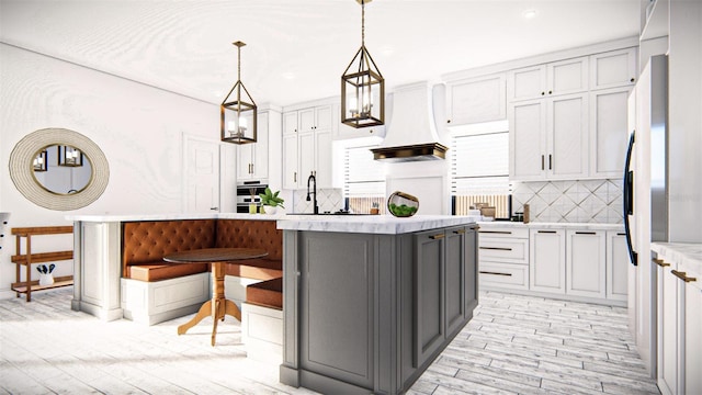 kitchen featuring premium range hood, a kitchen island, decorative light fixtures, backsplash, and light hardwood / wood-style floors