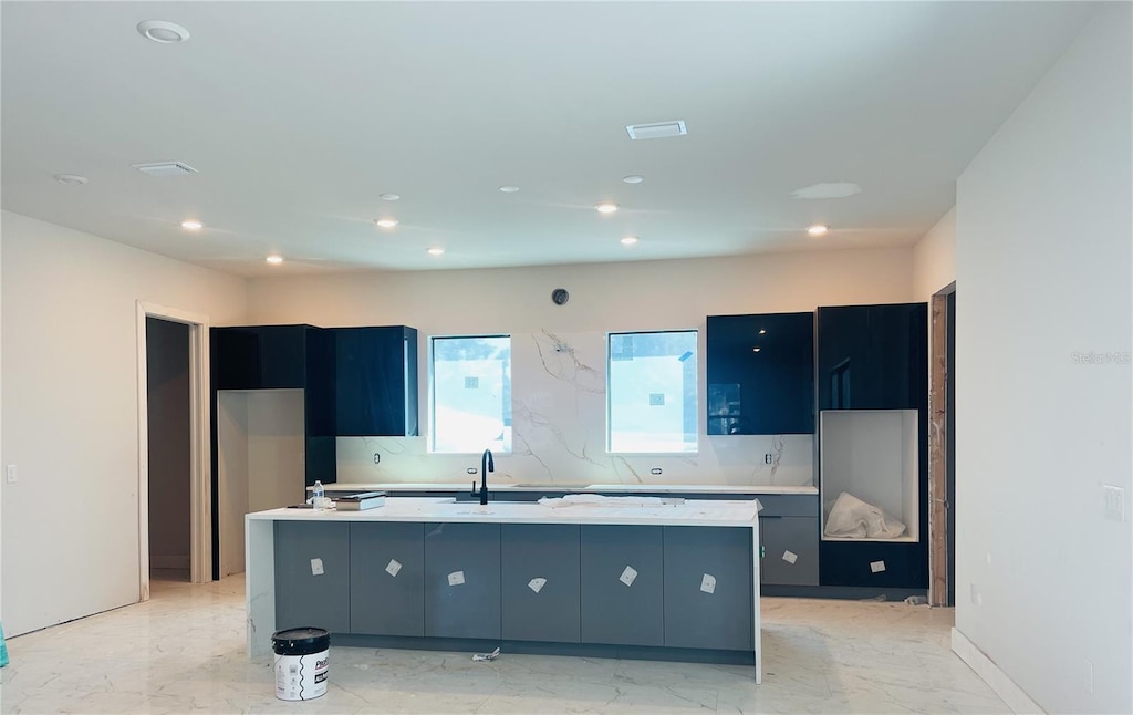 kitchen with marble finish floor, a center island with sink, light countertops, and a sink