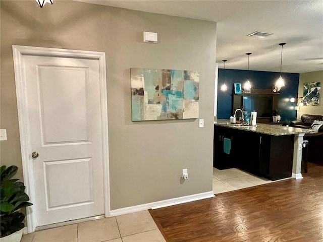 kitchen featuring light wood-type flooring, light stone countertops, sink, and decorative light fixtures