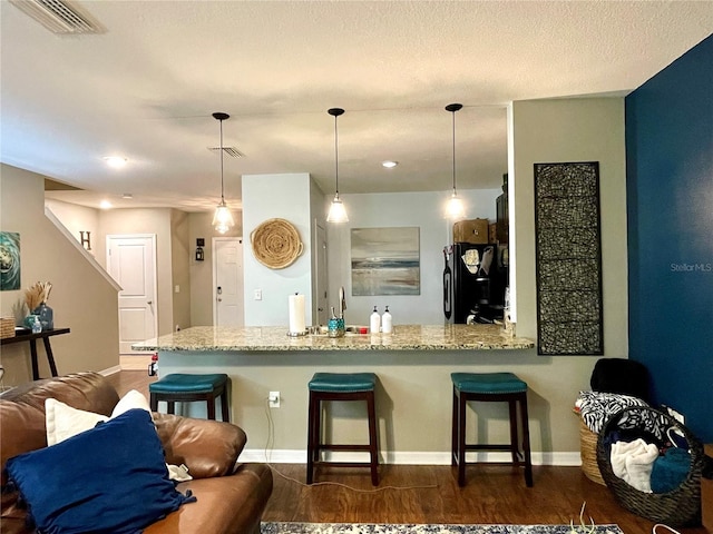 kitchen with hanging light fixtures, light stone counters, kitchen peninsula, a breakfast bar area, and black fridge