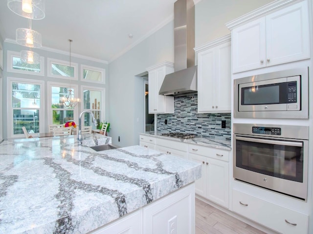 kitchen featuring ornamental molding, wall chimney range hood, stainless steel appliances, and white cabinets