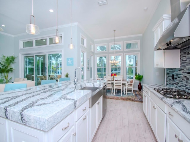 kitchen featuring white cabinetry, tasteful backsplash, wall chimney exhaust hood, a kitchen island with sink, and sink