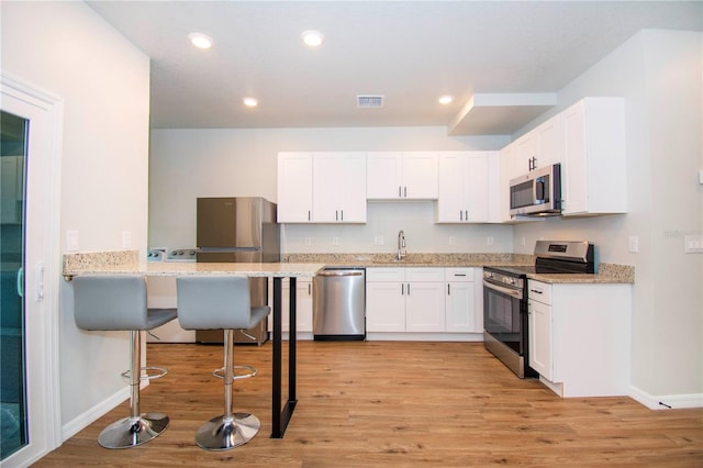 kitchen with light stone countertops, appliances with stainless steel finishes, light hardwood / wood-style flooring, white cabinetry, and a breakfast bar area