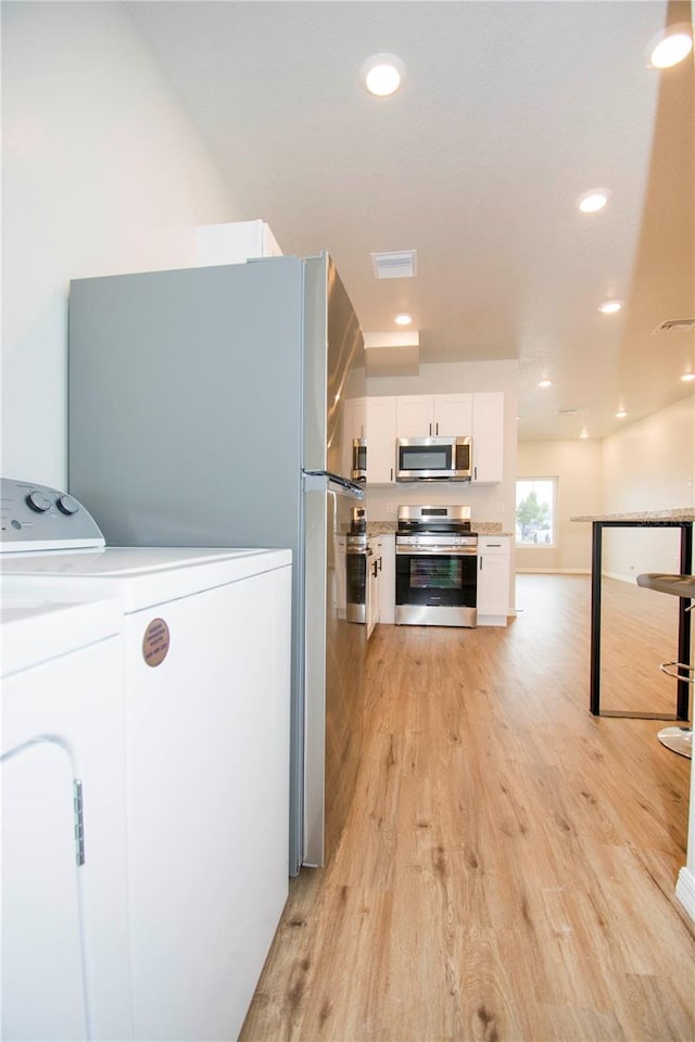 kitchen featuring white cabinets, washer and dryer, stainless steel appliances, and light hardwood / wood-style flooring