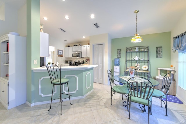 kitchen with white cabinets, kitchen peninsula, stainless steel appliances, light tile patterned floors, and decorative light fixtures