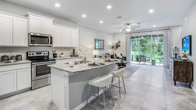 kitchen featuring ceiling fan, white cabinets, a center island with sink, and appliances with stainless steel finishes