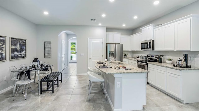 kitchen featuring light stone counters, a kitchen island with sink, white cabinets, a kitchen bar, and stainless steel appliances