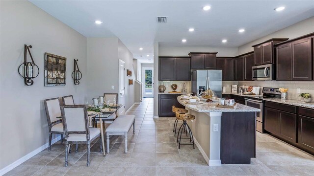 kitchen with dark brown cabinets, a center island, appliances with stainless steel finishes, and light stone counters