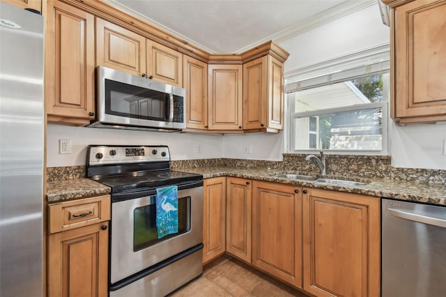 kitchen with ornamental molding, sink, appliances with stainless steel finishes, and dark stone counters