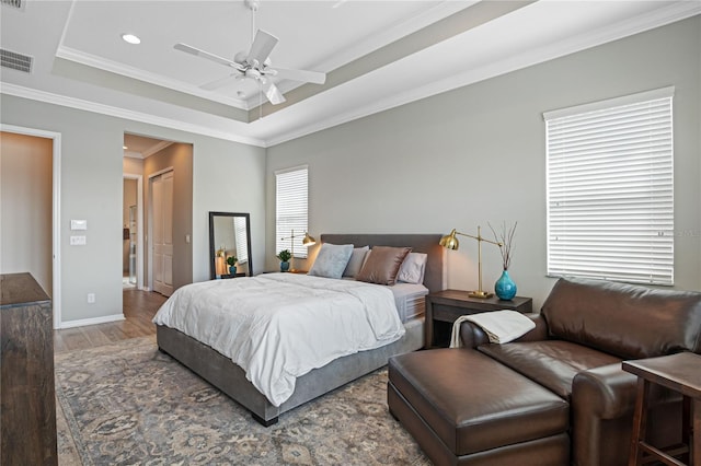 bedroom with hardwood / wood-style floors, ceiling fan, crown molding, and a tray ceiling