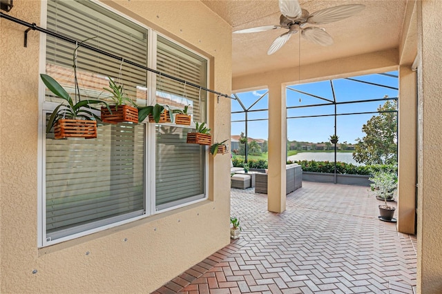 view of patio / terrace with ceiling fan, a water view, an outdoor hangout area, and glass enclosure