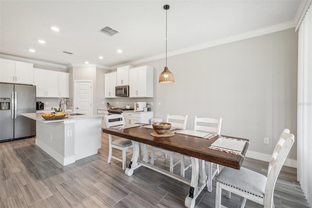 kitchen featuring sink, decorative light fixtures, a kitchen island with sink, white cabinetry, and appliances with stainless steel finishes