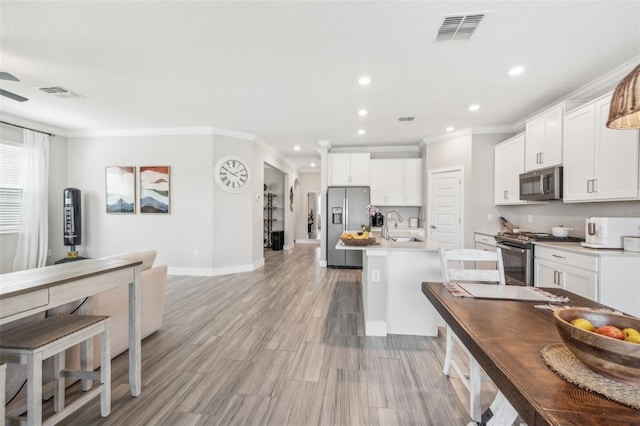 kitchen featuring appliances with stainless steel finishes, white cabinetry, an island with sink, light wood-type flooring, and crown molding