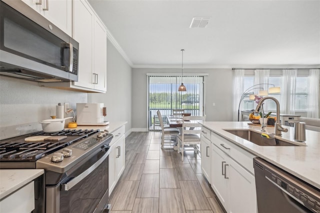 kitchen with sink, white cabinets, hanging light fixtures, stainless steel appliances, and ornamental molding