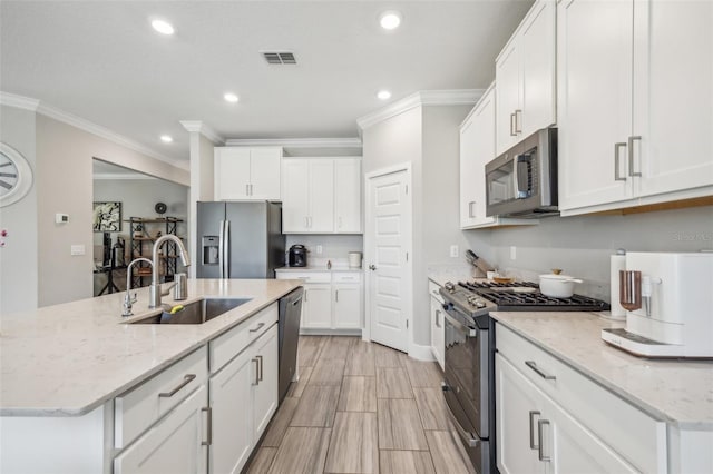 kitchen featuring white cabinetry, stainless steel appliances, a center island with sink, ornamental molding, and sink