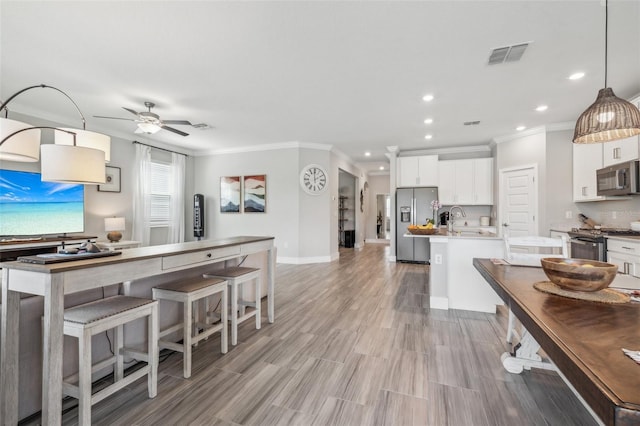 kitchen with white cabinets, an island with sink, sink, decorative light fixtures, and appliances with stainless steel finishes