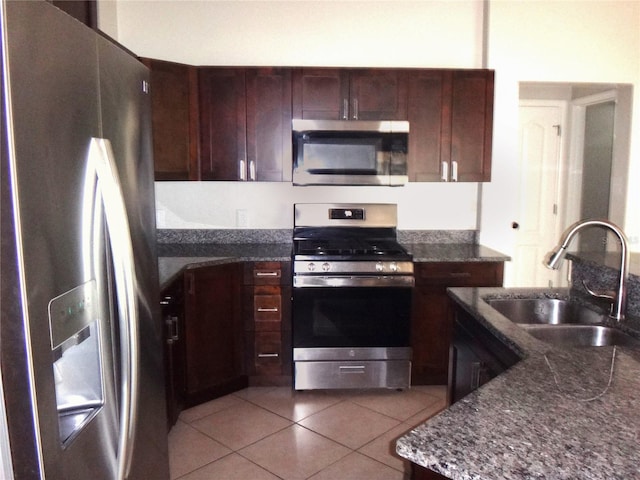 kitchen featuring sink, appliances with stainless steel finishes, dark brown cabinetry, light tile patterned floors, and dark stone countertops