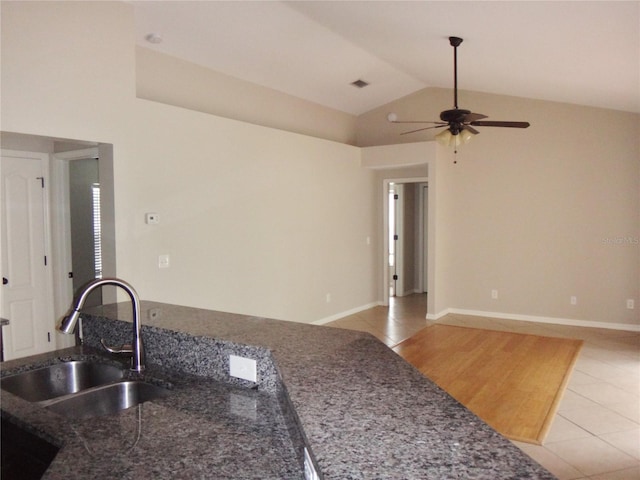 kitchen featuring dark stone countertops, vaulted ceiling, light tile patterned floors, ceiling fan, and sink