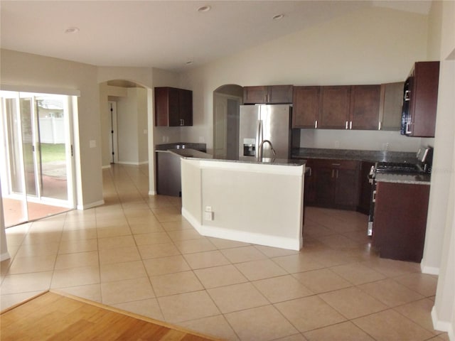 kitchen featuring light tile patterned flooring, an island with sink, stainless steel appliances, lofted ceiling, and dark brown cabinetry