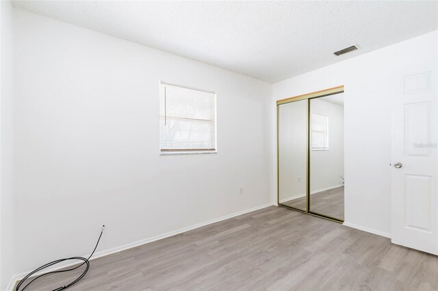 unfurnished bedroom featuring light hardwood / wood-style floors, a closet, and a textured ceiling