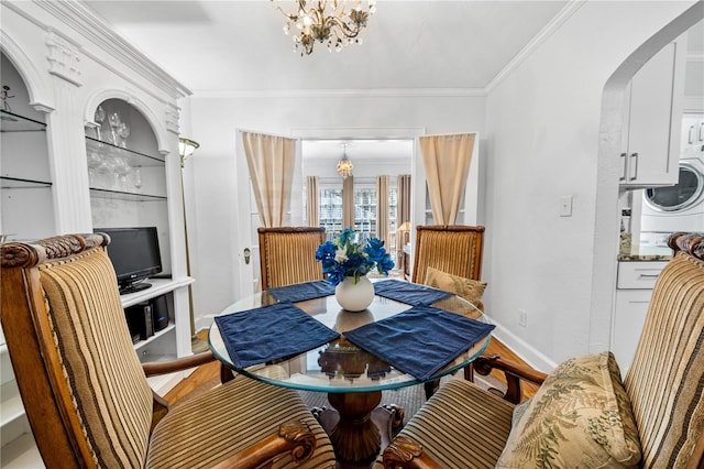 dining room featuring stacked washer / dryer, crown molding, wood-type flooring, and a notable chandelier