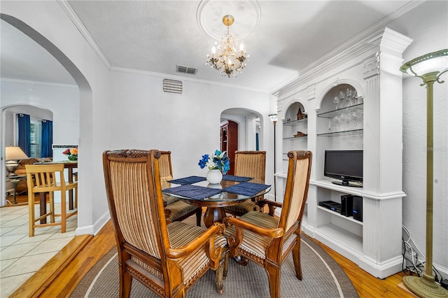 dining space featuring light hardwood / wood-style flooring, built in shelves, ornamental molding, and an inviting chandelier