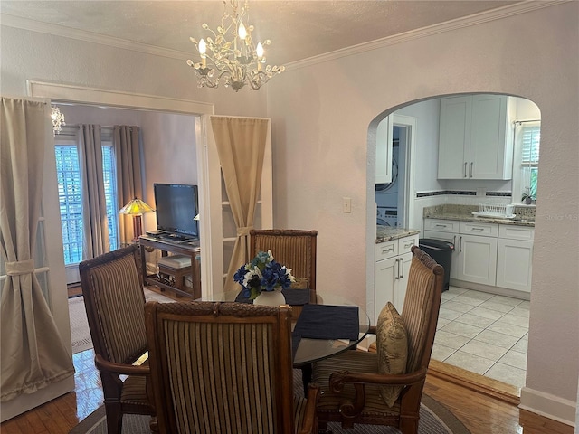 dining area with crown molding, a notable chandelier, arched walkways, and light wood-type flooring