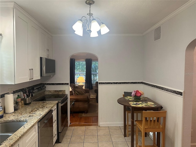 kitchen with light tile patterned floors, visible vents, arched walkways, appliances with stainless steel finishes, and wainscoting