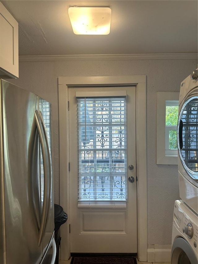 doorway with stacked washing maching and dryer, crown molding, and a textured wall