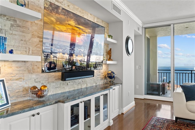 bar with white cabinets, dark hardwood / wood-style flooring, dark stone counters, ornamental molding, and a water view