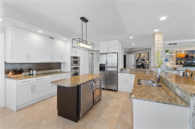 kitchen with a kitchen island with sink, hanging light fixtures, sink, white cabinets, and appliances with stainless steel finishes