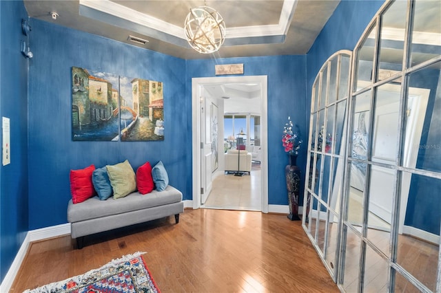 sitting room with ornamental molding, an inviting chandelier, hardwood / wood-style floors, and a tray ceiling