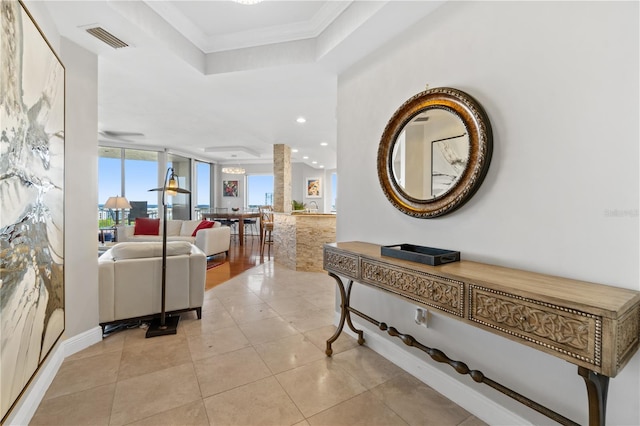 hallway with crown molding, a tray ceiling, and light tile patterned floors