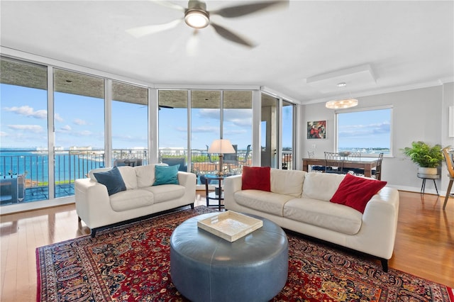 living room featuring ceiling fan with notable chandelier, hardwood / wood-style floors, a wall of windows, a water view, and ornamental molding