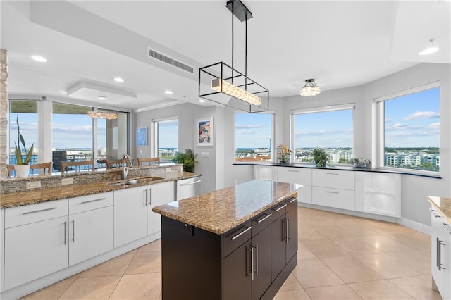 kitchen featuring a kitchen island, hanging light fixtures, sink, light stone countertops, and white cabinetry