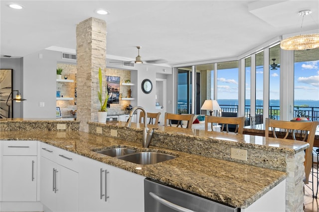 kitchen with a breakfast bar area, decorative columns, stainless steel dishwasher, white cabinets, and a water view