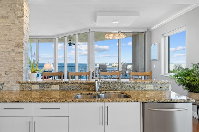 kitchen with ornamental molding, sink, stone counters, white cabinetry, and a water view