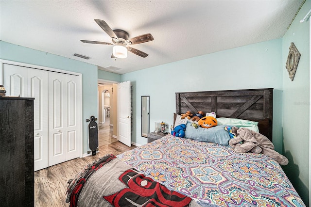 bedroom with a closet, light hardwood / wood-style floors, ceiling fan, and a textured ceiling