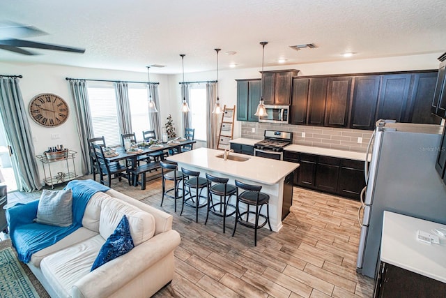 kitchen with backsplash, a kitchen island with sink, sink, hanging light fixtures, and appliances with stainless steel finishes