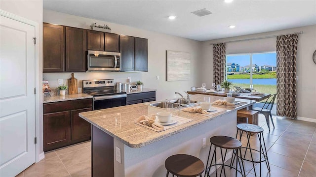 kitchen with appliances with stainless steel finishes, dark brown cabinetry, sink, and an island with sink