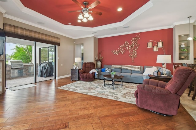 living room with a raised ceiling, crown molding, hardwood / wood-style floors, and ceiling fan