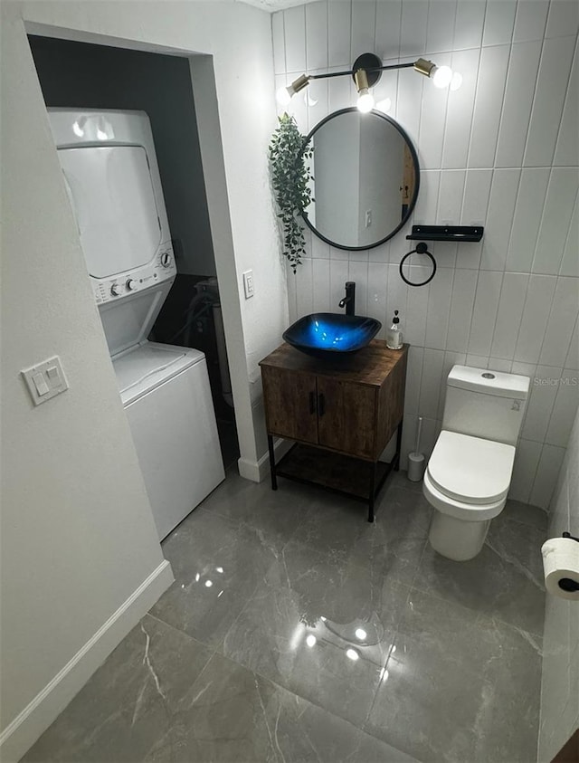 interior space with stacked washer / drying machine, toilet, tile walls, and vanity